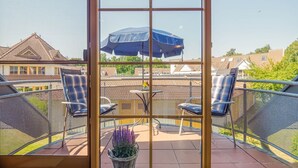 A balcony with two chairs, a table, and a blue umbrella. - Comfortable Windrose vacation apartment with balcony, pool and garden view in Zingst - (Zingst)