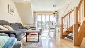 A modern living room with a sofa, a coffee table, and a staircase. - Comfortable Windrose vacation apartment with balcony, pool and garden view in Zingst - (Zingst)