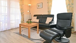 Un salon avec un canapé, un fauteuil en cuir noir, une table basse en bois et une lampe.