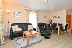 Uma sala de estar moderna com um sofá de couro preto, uma mesa de centro de madeira e uma área de jantar com cadeiras de couro preto e uma mesa de madeira.