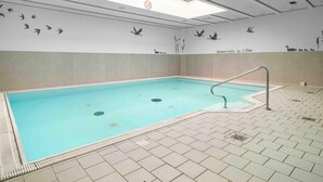 Une piscine intérieure avec un sol carrelé, une rambarde et des peintures murales représentant des oiseaux et des roseaux.