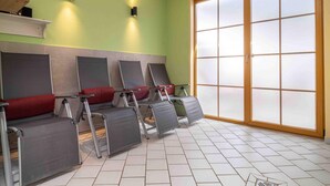 Une pièce avec un mur vert, une grande fenêtre à vitres dépolies et plusieurs fauteuils inclinables dotés de coussins rouges.