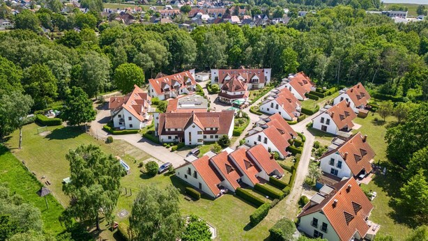 Vue aérienne d’un quartier résidentiel avec des maisons, des pelouses verdoyantes et une grande étendue d’eau en arrière-plan.