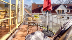 Un balcón con una mesa dispuesta para dos personas, una sombrilla roja y vistas a casas vecinas.