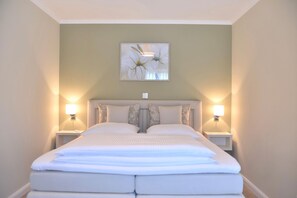 A neatly made bed in a room with two bedside lamps, a framed floral artwork above the bed, and a light green wall. - Modern apartment with balcony and limited sea view in Zingst - (Zingst)