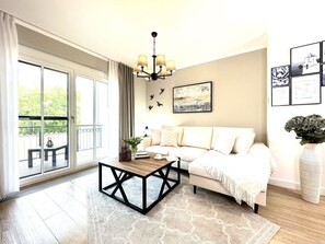 A spacious living room with a large sliding glass door leading to an outdoor balcony, a modern coffee table, a sofa with a throw blanket, and a chandelier. - Modern vacation apartment Strandperle in Zingst with balcony - Logierhaus Friedrich (Zingst)