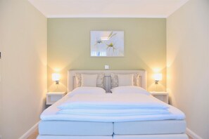 A neatly made double bed with a headboard, two bedside lamps, and a wall-mounted artwork above. - Modern vacation apartment Strandperle in Zingst with balcony - Logierhaus Friedrich (Zingst)