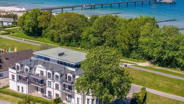Un edificio moderno de dos pisos con techo plano y ventanas amplias, situado cerca de la costa con un muelle que se adentra en el agua.