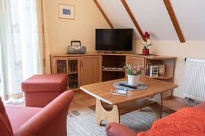 Una sala de estar acogedora con una mesa de madera, un sofá rojo y un televisor sobre un mueble.