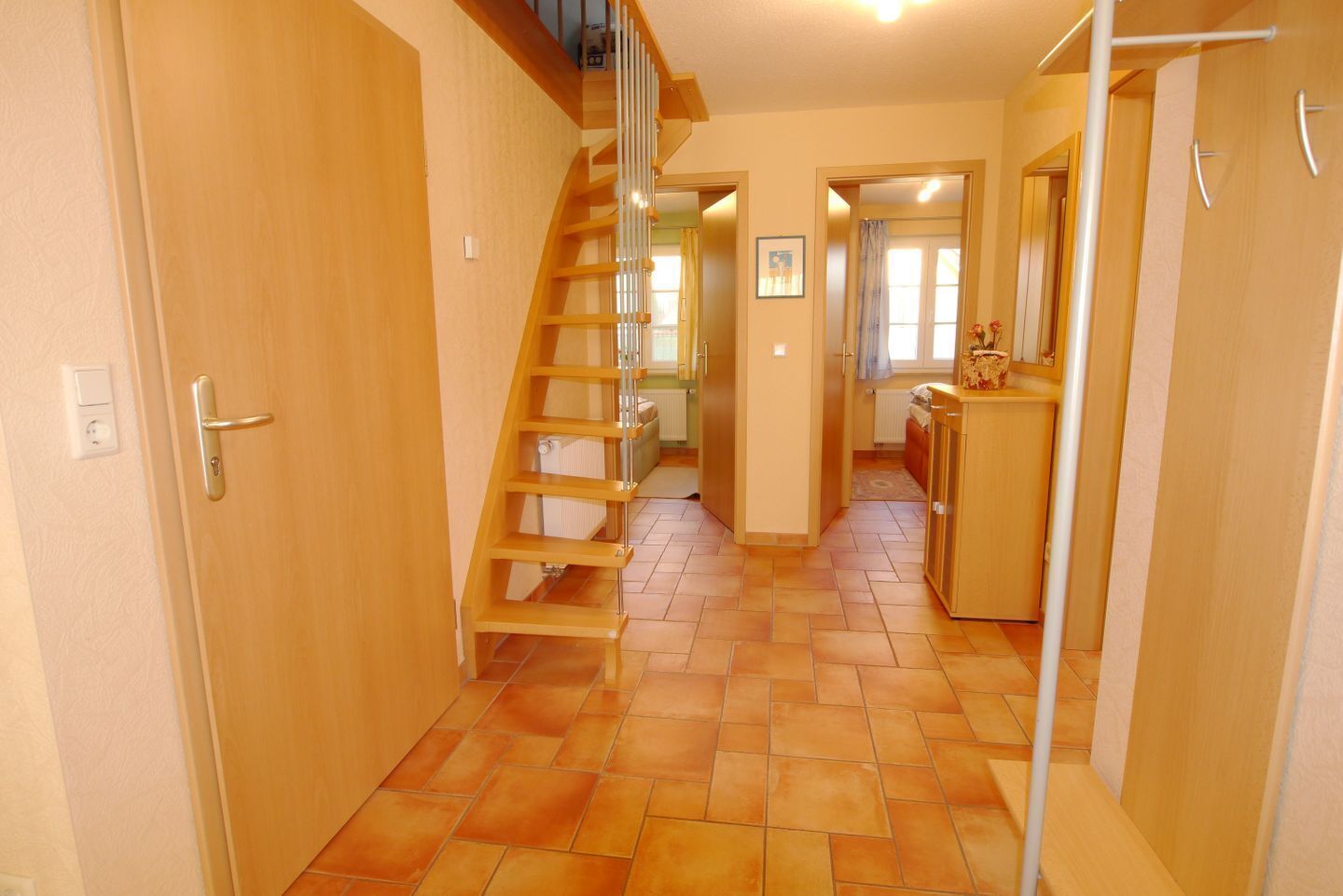 Ein schmaler Flur mit einer Holztreppe, einer Tür mit Griff und einem Heizkörper an der Wand.
