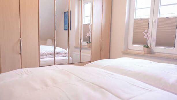 A bedroom with a bed, a wardrobe, and a window with blinds. - Haus Sabine - Upper floor - Bright, large upper floor apartment in a quiet location! (Zingst)