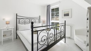 Une chambre à coucher avec un lit à baldaquin, une table de chevet avec une lampe, une fenêtre avec des rideaux et un radiateur.