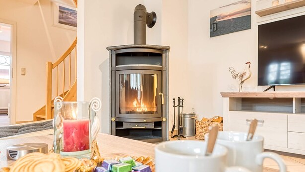 Un salon chaleureux avec un poêle à bois, une télévision et un coin repas où une table est dressée pour le repas.