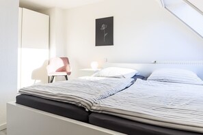 Une chambre à coucher comprenant un lit, une chaise, une table de chevet et un tableau accroché au mur.