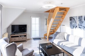 En moderne stue med TV, sofa, sofabord og en trappe i træ.