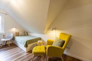 Ein Schlafzimmer mit einem Bett, einem gelben Sessel, einem kleinen Tisch und einer Lampe.