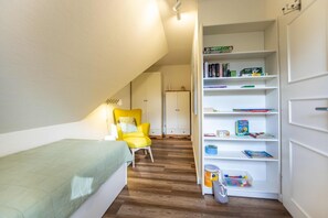 A small, cozy room with a single bed, a yellow chair, and a bookshelf filled with books and toys. - Vacation apartment Klintum - pure idyll and very quiet (Oldsum)