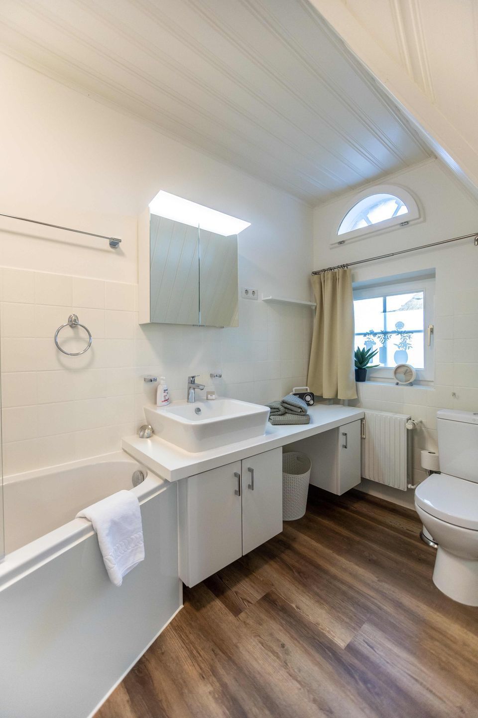 Une salle de bain équipée d’une baignoire, d’un lavabo, d’un meuble-lavabo et de toilettes. Une fenêtre offre une vue sur l’extérieur.