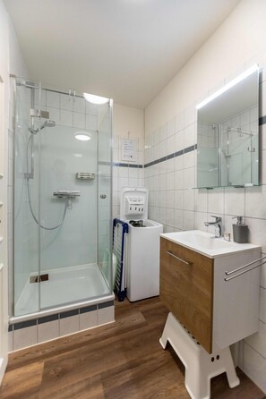 Ein modernes Badezimmer mit einer gläsernen Dusche, einem weißen Waschbecken mit Holzunterschrank und einem großen Spiegel darüber.