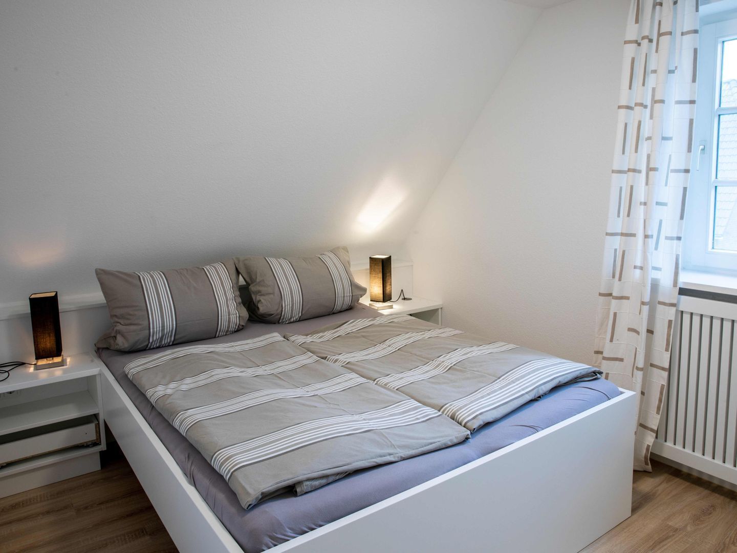 A bedroom with a bed, bedside tables, a lamp, and a window with curtains.
