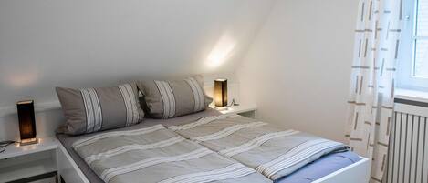 A bedroom with a bed, bedside tables, a lamp, and a window with curtains.