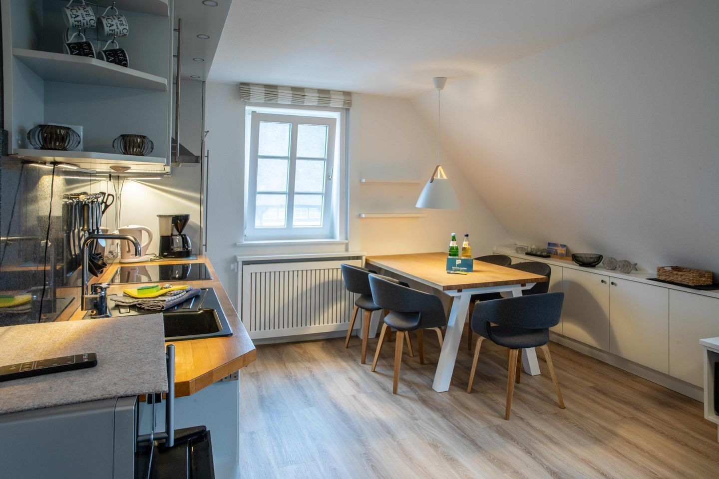 Une petite cuisine avec une table en bois, des chaises, une fenêtre et un radiateur.