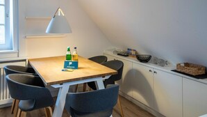 A small dining area with a wooden table, four grey chairs, a white pendant lamp, and a white cabinet with a basket and decorative items. - Vacation apartment Wrixumer Marsch - Located directly on the marsh (Wrixum)