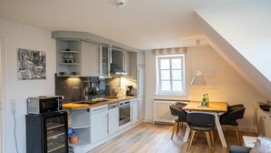 A compact kitchen with a microwave, oven, and coffee maker. There is a dining area with a table and chairs, and a small seating area with a sofa. - Vacation apartment Wrixumer Marsch - Located directly on the marsh (Wrixum)