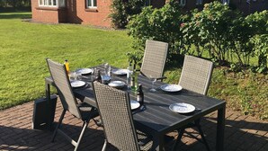 A brick house with a thatched roof, a table set for dining, and outdoor chairs. - Ferienwohnung Britta (Wyk auf Föhr)