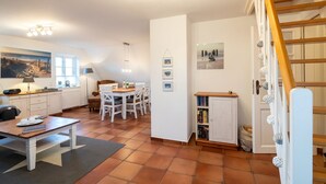 A compact living space with a dining area, a kitchen, a staircase, and a bookshelf. - Ferienwohnung Britta (Wyk auf Föhr)