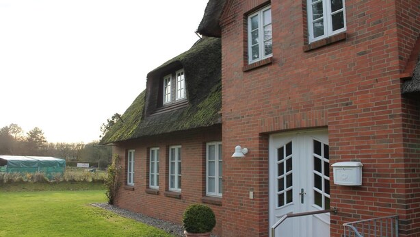 A red brick house with a white door and windows, a small garden, and a green shed in the background. - Ferienwohnung Britta (Wyk auf Föhr)