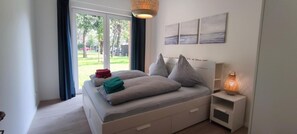 Ein Schlafzimmer mit einem Bett, einem Nachttisch, einer Lampe und Blick ins Freie.