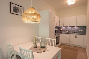 Una cocina moderna con armarios blancos, una mesa de comedor con sillas, una lámpara colgante y un cuadro en la pared.