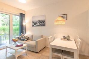 Ein modernes Wohnzimmer mit einer Couch, einem Esstisch und Stühlen. Es gibt ein Fenster mit Vorhängen, ein Wandbild und eine Pendelleuchte.
