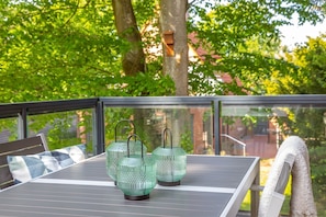 Une table sur laquelle reposent deux lanternes en verre vert, sur un balcon offrant une vue sur les arbres.