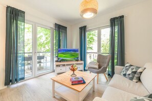 Una sala de estar moderna con una televisión, una mesa de centro con libros, un sofá y un sillón.