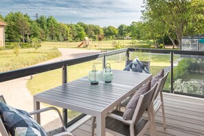 Eine Terrasse mit Tisch und Stühlen, mit Blick auf eine Wiese mit Spielplatz und Bäumen.