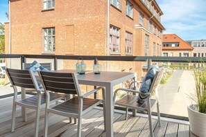 Un balcón con una mesa y sillas de madera, una planta en maceta y vista a un edificio de ladrillo.