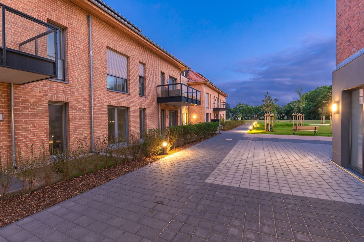 A brick building with a paved walkway, a bench, and a well-lit outdoor area.