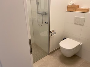 Um banheiro moderno com chuveiro de vidro, vaso sanitário e prateleira com artigos de higiene.