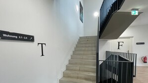 A staircase with a black railing, a sign indicating room 2.1-2.4, and a fire extinguisher on the wall.