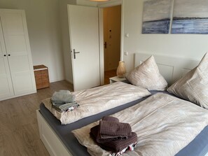 Quarto com duas camas, guarda-roupa, mesa de cabeceira com abajur e um quadro na parede.