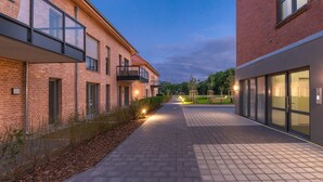 A pathway between two buildings with brick facades, a paved walkway, and outdoor lighting.