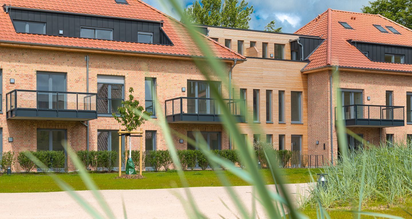 A modern multi-story residential building with brick walls, large windows, and a red-tiled roof.