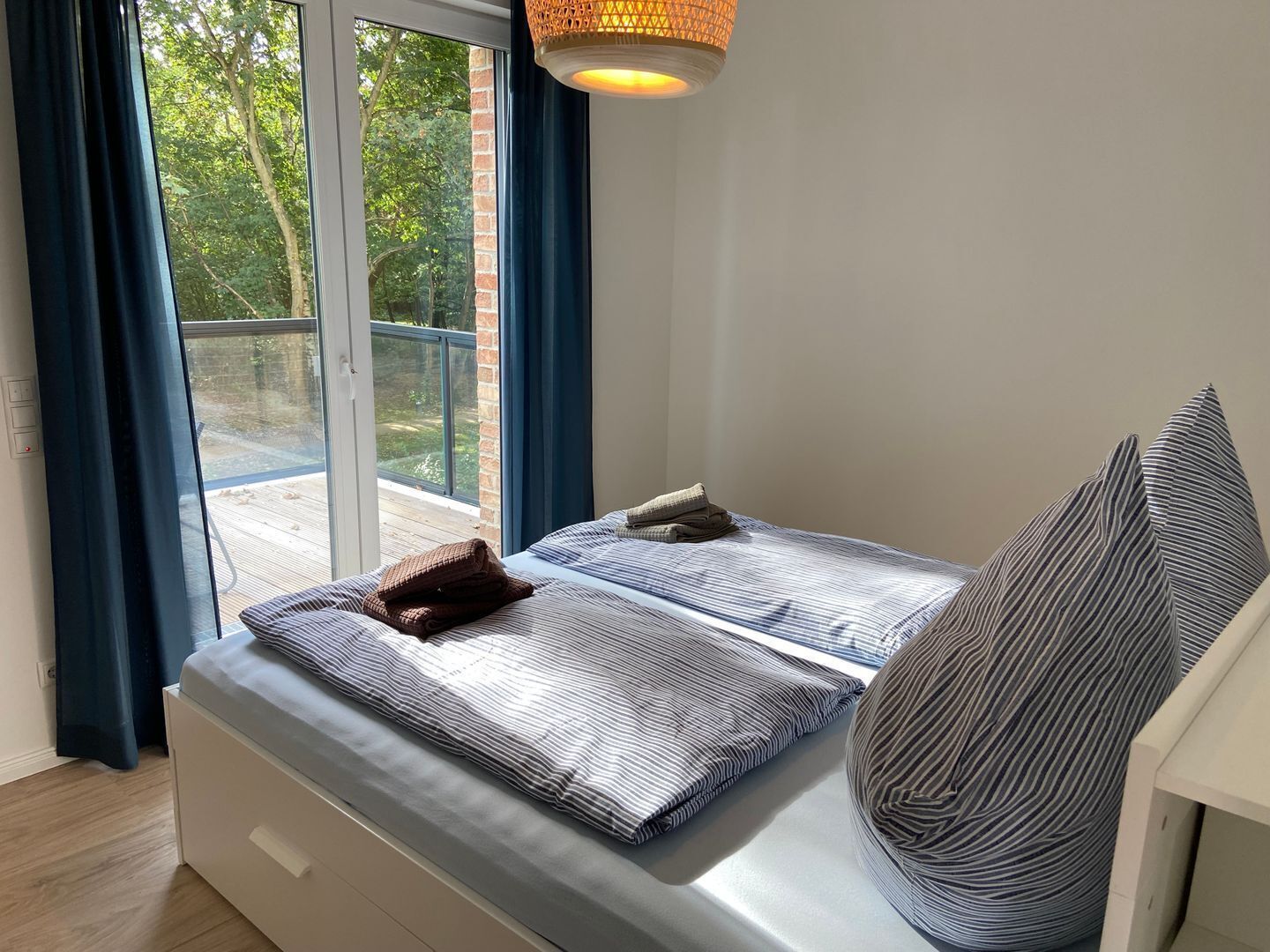 A bedroom with a large window, a bed with striped bedding, and a hanging light fixture.