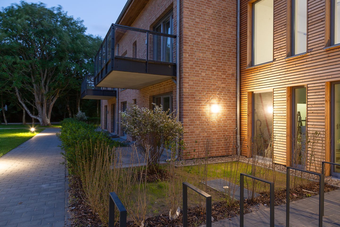 A modern two-story building with a brick facade, a balcony, and a well-lit entrance.