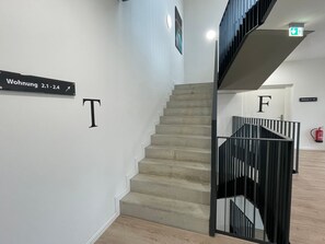 A staircase with a black railing, a sign indicating room 2.1-2.4, and a fire extinguisher on the wall.