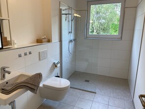 Un baño moderno con ducha, inodoro, lavamanos y ventana con vistas a árboles.