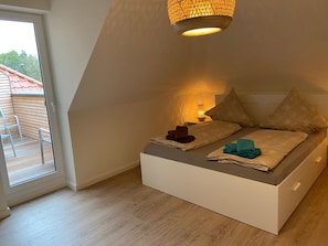 A bedroom with a loft bed, a small bedside table with a lamp, and a view of the outside balcony.