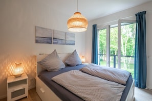 Un dormitorio con una cama grande, dos lámparas de noche y vistas a la vegetación por la ventana.